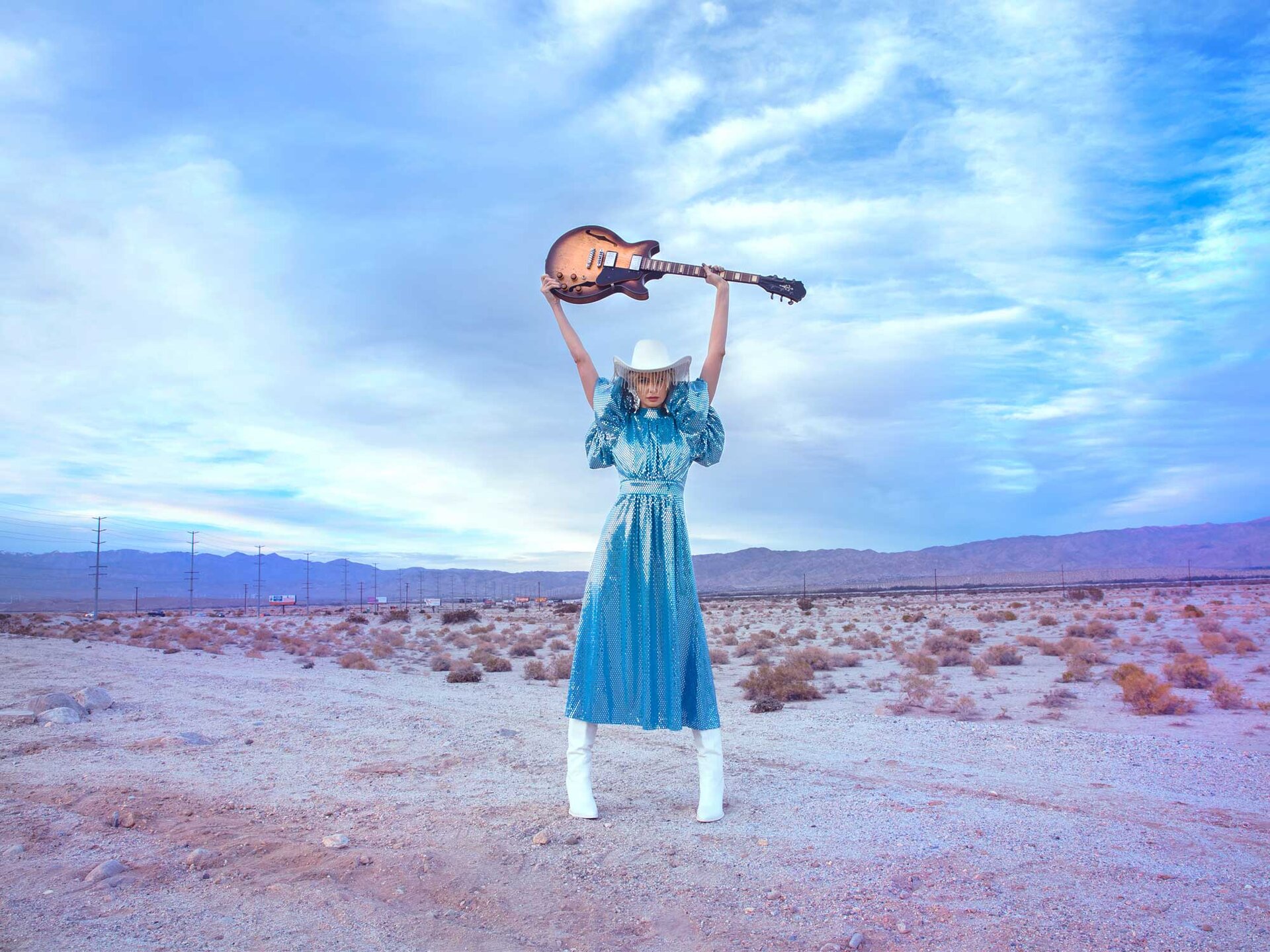 girl holding guitar over head in desert